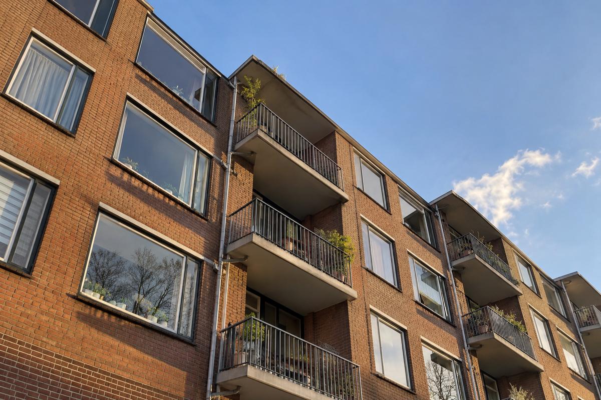 Bakstenen appartementengebouw met balkons en planten, van onderaf gezien in de middagzon